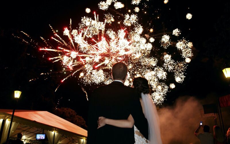 Happy hugging bride and groom watching beautiful colorful fireworks night sky