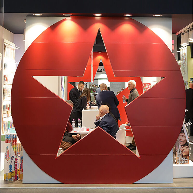 Persone conversano all'interno di una struttura espositiva con grande stella rossa, in fiera commerciale.