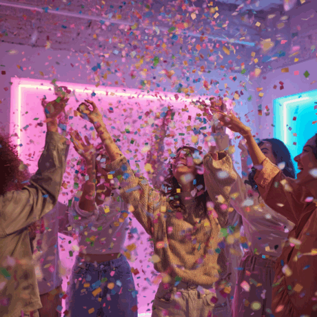 Persone che celebrano sotto una pioggia di coriandoli colorati in una stanza illuminata da luci al neon.