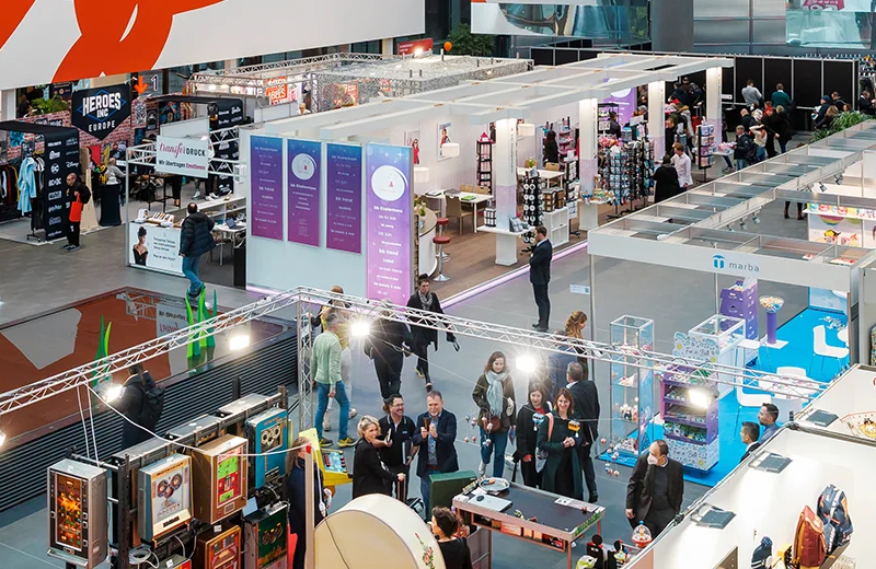 Header_Standbau Vista dall'alto di una fiera commerciale con stand espositivi e persone che camminano e interagiscono.